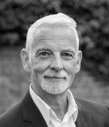 Black and white image of board member, Kieron James smiling at the camera