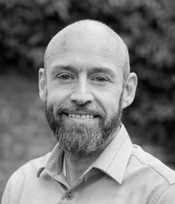 Black and white image of board member, Nick Jones, smiling towards the camera