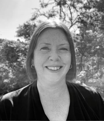 black and white image of Andrea Gregory smiling in front of some foliage
