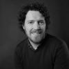 An image of Conor Gibson smiling to camera in front of a plain wall